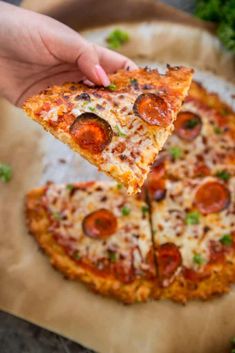 a slice of pizza being held up by someone's hand over a piece of parchment paper