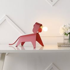 a pink dog lamp sitting on top of a white shelf next to a vase with flowers