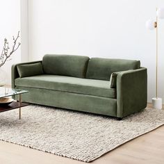 a green couch sitting on top of a wooden floor next to a glass coffee table