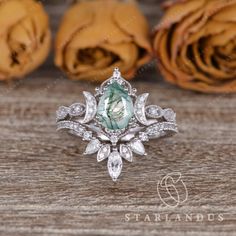 an engagement ring with a green stone surrounded by white diamonds on a wooden table next to roses