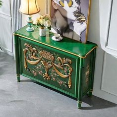 a green cabinet with a painting on the top and flowers in vases next to it