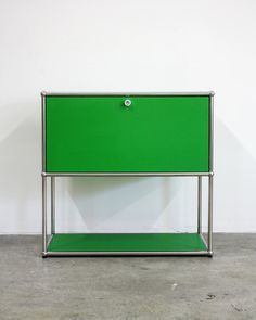 a green cabinet sitting on top of a cement floor next to a white wall with a metal frame