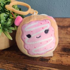 a pink donut keychain sitting on top of a wooden table next to a potted plant