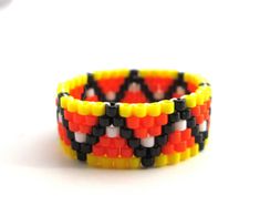 an orange, yellow and black beaded bracelet on a white surface with a small object in the background