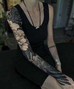 a woman sitting on the floor with her arm covered in flowers and leaves, wearing a black dress