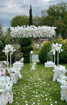 an outdoor ceremony setup with white flowers and petals on the grass in front of it