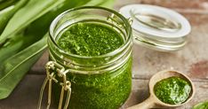 a jar filled with green pestle next to a wooden spoon and leafy greens