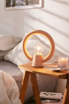 a wooden table with a light on top of it next to a bed and pillows