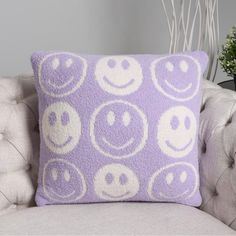 a purple pillow with smiley faces on it sitting on a chair next to a potted plant