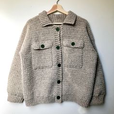 a sweater with buttons is hanging on a hanger against a white wall and it has a green button in the middle