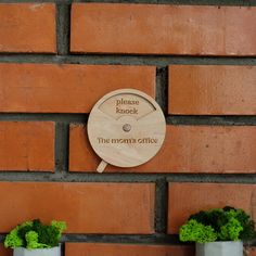 a clock mounted to the side of a brick wall next to two potted plants