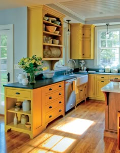 a kitchen with yellow cabinets and black counter tops, wooden floors, and open shelving