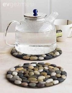 a glass tea pot and coaster on a table with rocks in front of it,