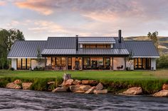 a large house sitting next to a river in the middle of a lush green field