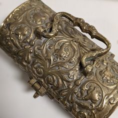 an old metal box with ornate designs on it's sides and handles, sitting on a white surface