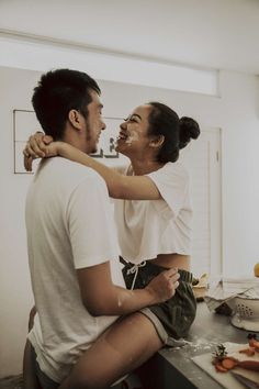 a man and woman are sitting on the kitchen counter, one is holding his arm around the other's neck