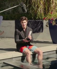 a young man sitting on the edge of a swimming pool with his feet in the water