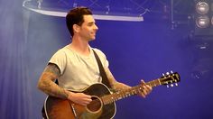 a man holding a guitar while standing on top of a stage with blue lights behind him