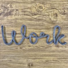 the word work written in blue yarn on a wooden surface