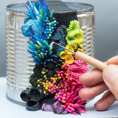 a person is holding a pencil and painting flowers on a tin can with paintbrushes