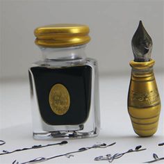 an old fashioned bottle with a gold cap next to a silver and black ink pen