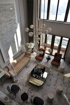 a living room filled with lots of furniture next to a tall glass window covered wall