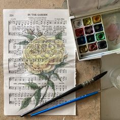 an open box of watercolor paints next to a paper with a rose on it