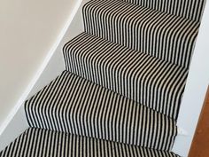 a cat sitting on top of a striped carpeted stair case