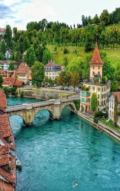 a river running through a lush green hillside next to a bridge with buildings on it