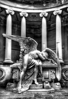 an angel statue sitting on top of a bench in front of some tall pillars and columns