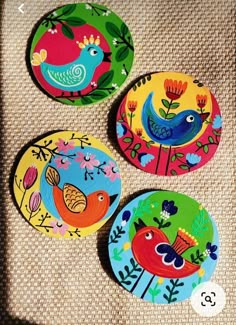 three colorful bird coasters sitting on top of a piece of cloth next to each other