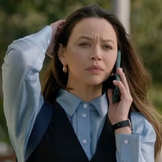 a woman holding a cell phone to her ear while wearing a blue shirt and black vest