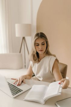 a woman sitting at a desk with a book and laptop