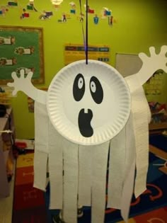 a paper plate with a ghost hanging from it's side on a string in front of a green wall