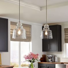 two lights hanging over a kitchen island with flowers in the vase and on the counter