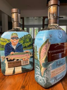 two bottles that have fish on them sitting on a wooden table in front of a window