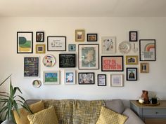 a living room filled with lots of framed pictures on the wall next to a couch