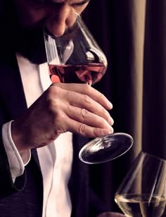 a man holding a glass of red wine in his right hand and looking down at it