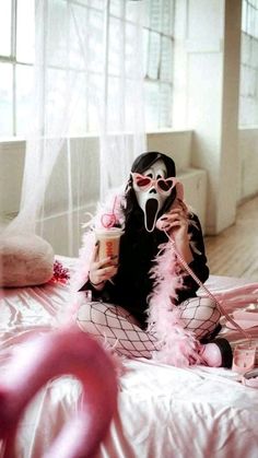 a woman sitting on top of a bed holding a drink in her hand and wearing makeup