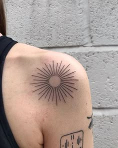 a woman with a tattoo on her shoulder has a sunburst in the middle