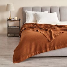 a bed with an orange blanket on top of it next to a night stand and lamp