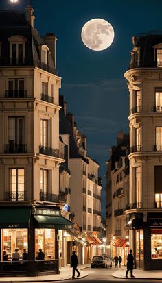 two people walking down the street in front of some buildings at night under a full moon