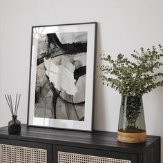 a black and white painting sitting on top of a wooden shelf next to a vase filled with flowers