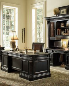 an office desk with two chairs and a bookcase in front of windows, along with a rug on the floor