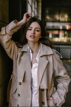 a woman leaning against a wall wearing a trench coat