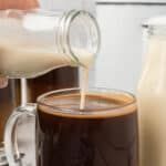 a person pouring milk into a glass mug