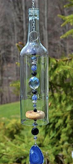 a glass bottle with beads hanging from it's side in front of some trees