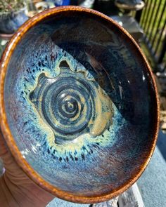 a hand holding a blue and yellow bowl with swirls in it's center