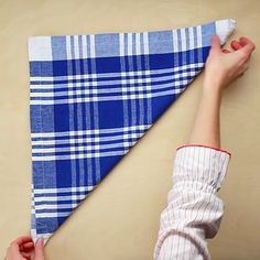 a person holding a blue and white checkered cloth on top of a wooden table