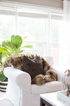 a white chair with a leopard print pillow on it in front of a large window